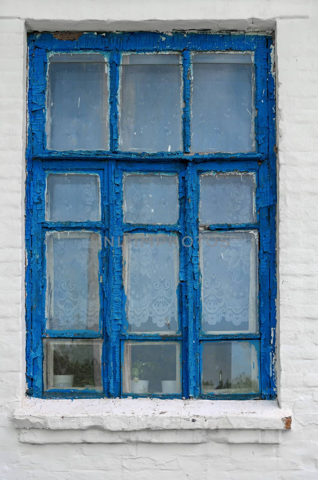 Ancient  window with peeling blue paint on a white wall.