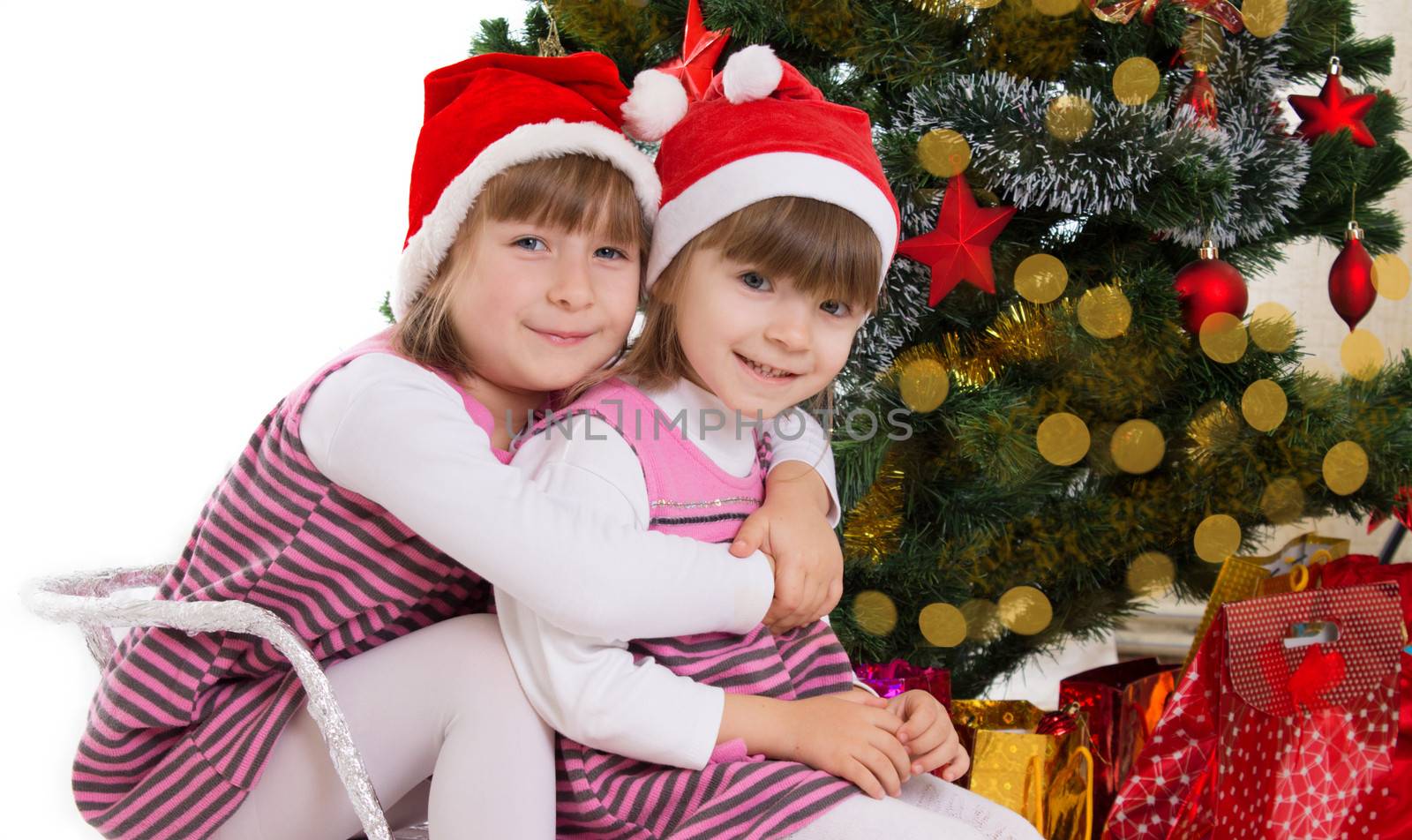 Sisters hugging in sledge under Christmas tree by Angel_a