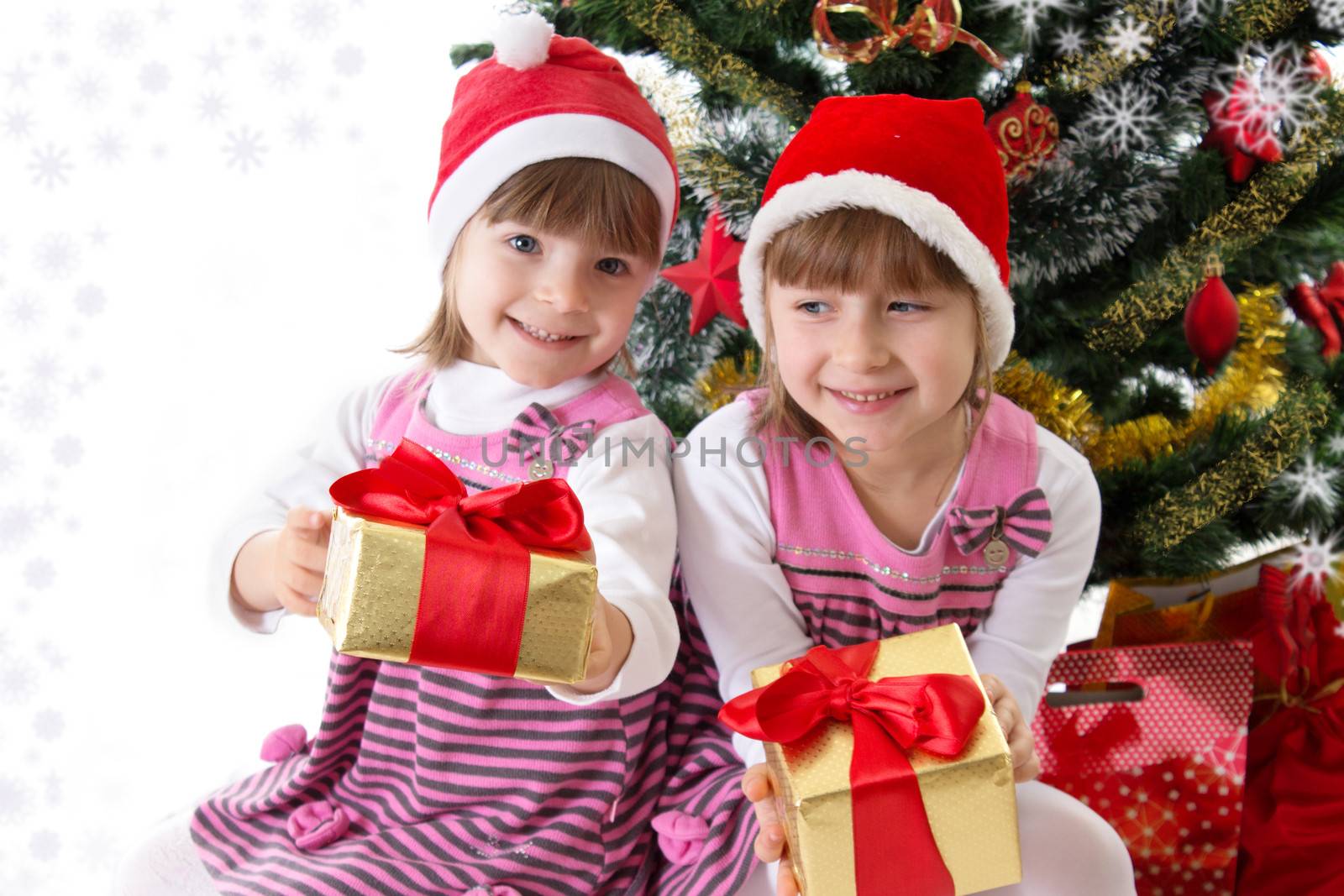 Two little sisters with gifts under Christmas tree over white