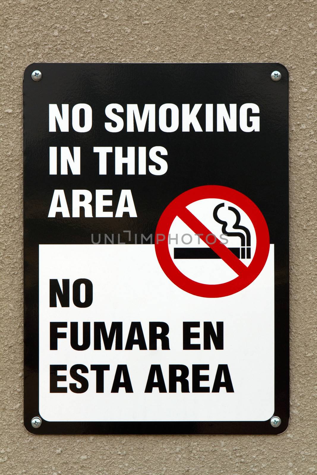Bilingual no smoking sign with graphic and written in the English and Spanish languages is screwed to a wall.