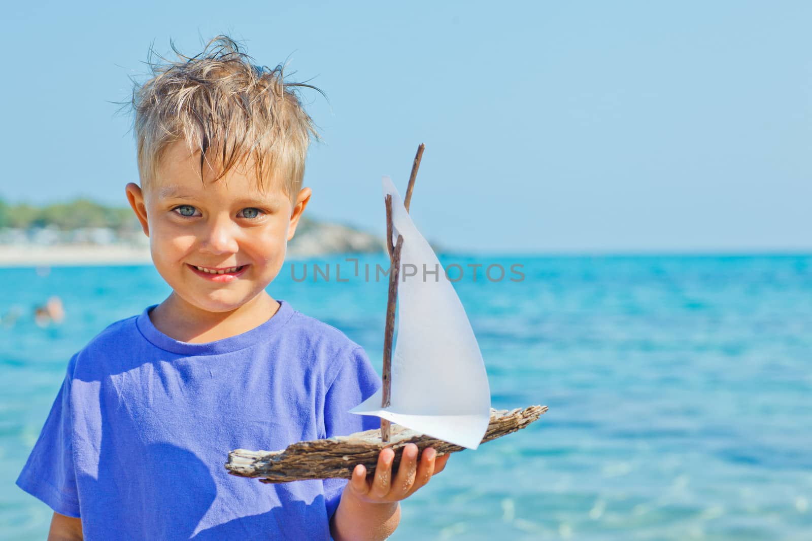 Cute boy with toy ship in hands ashore. Vertical view