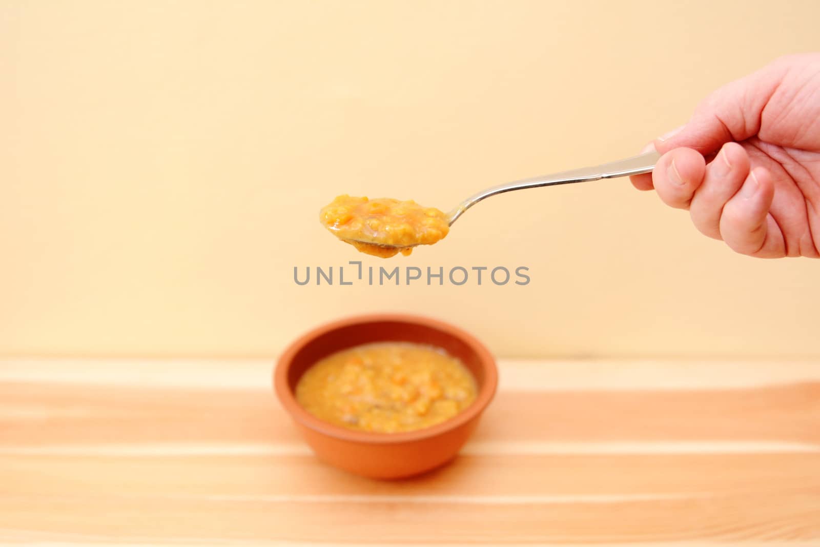Hand holding spoonful of soup above a bowl on a wooden table with copy space