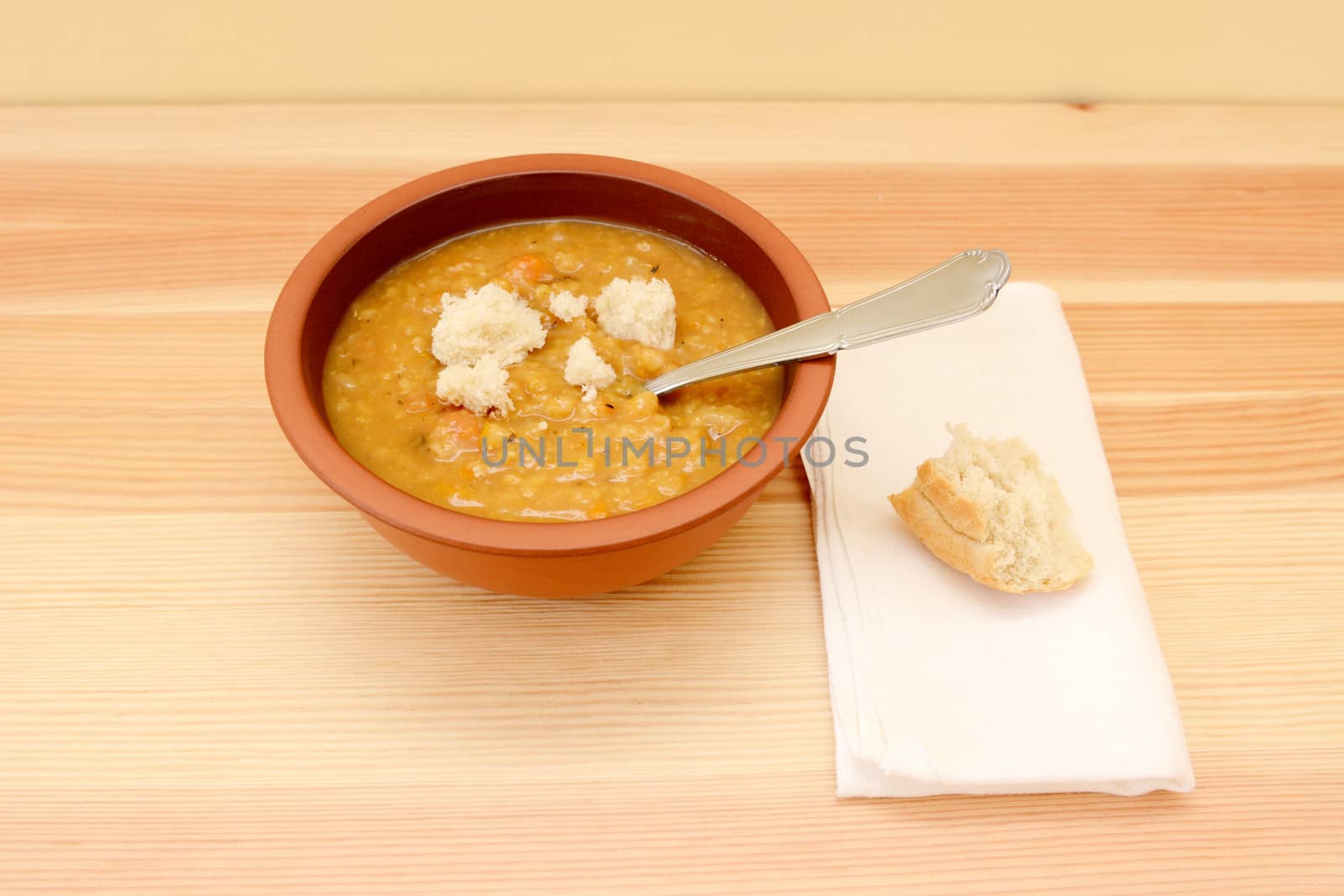Bowl of soup served with torn pieces of white bread roll on a linen napkin