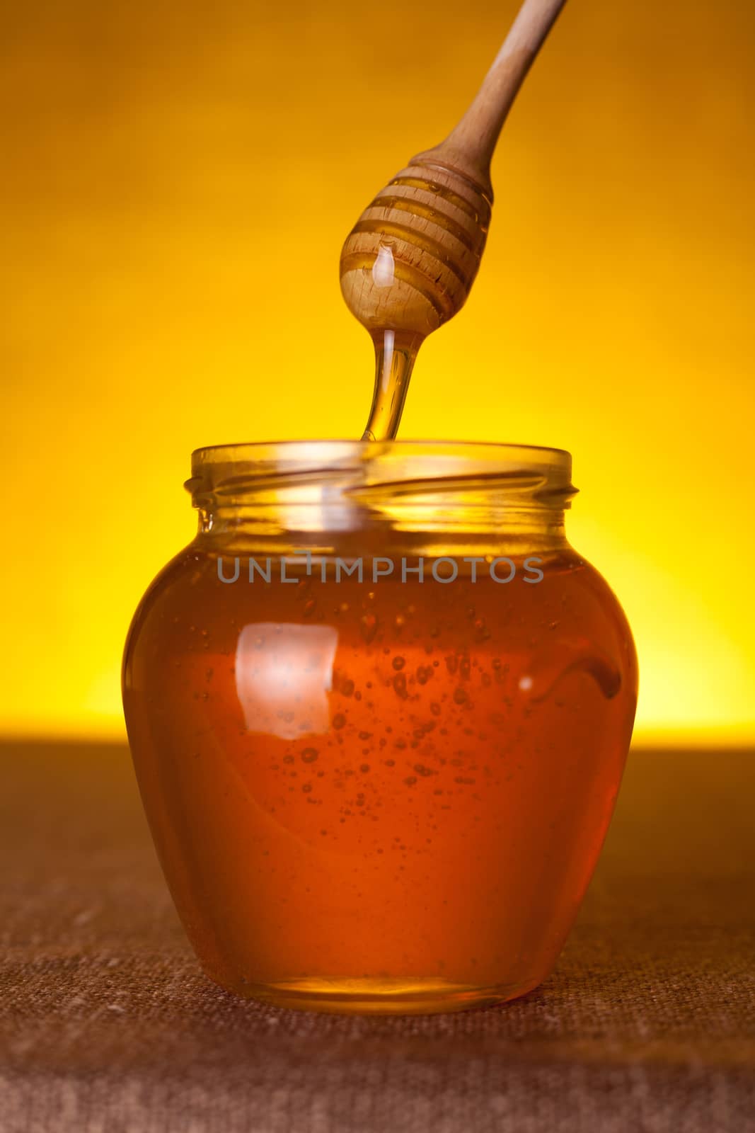 Honey jar with dipper and flowing honey, selective focus on dipper 