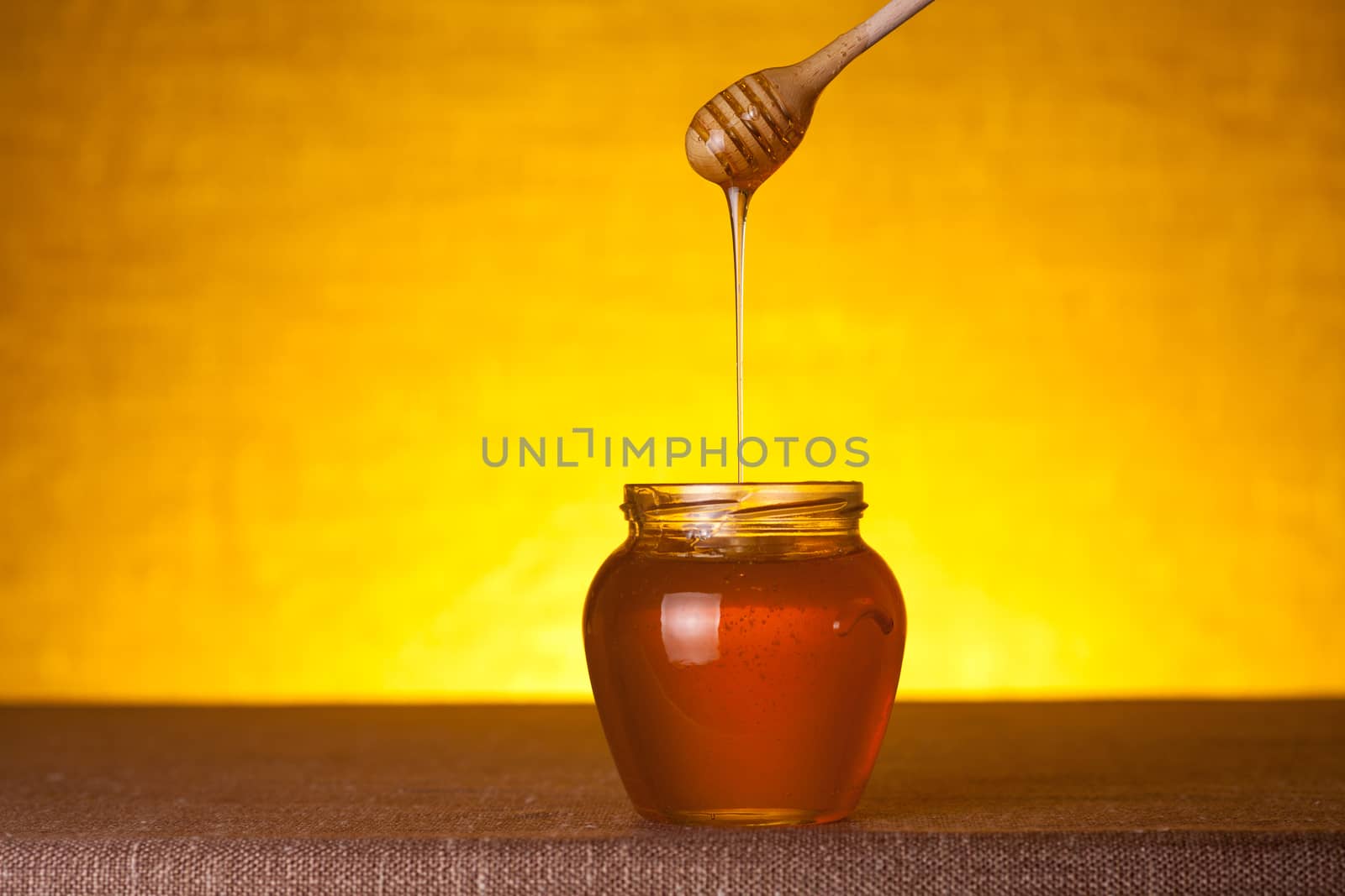 Honey jar with dipper and flowing honey, on canvas table 