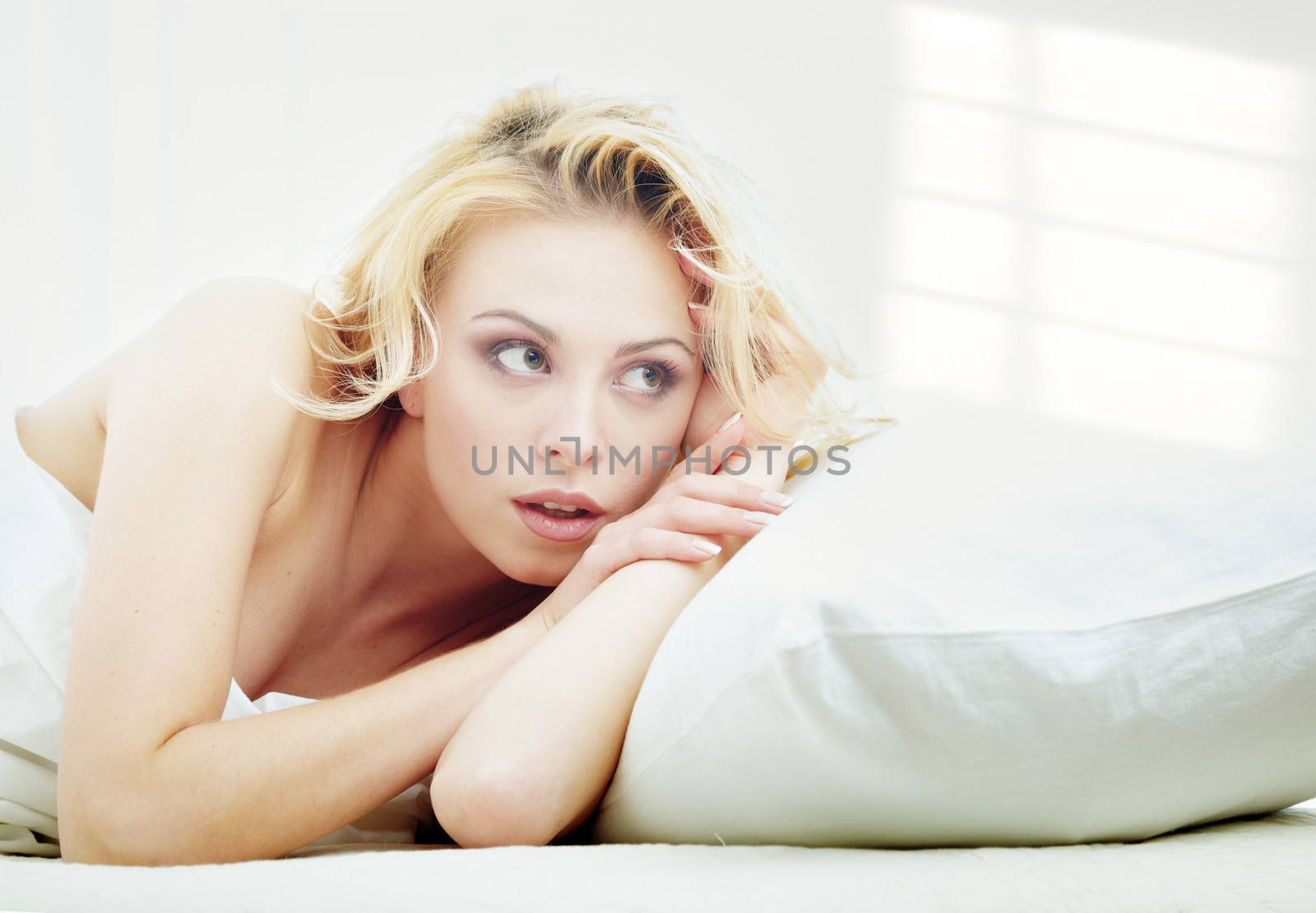 Young blond lady laying in a bedroom with shadows on the wall from the window