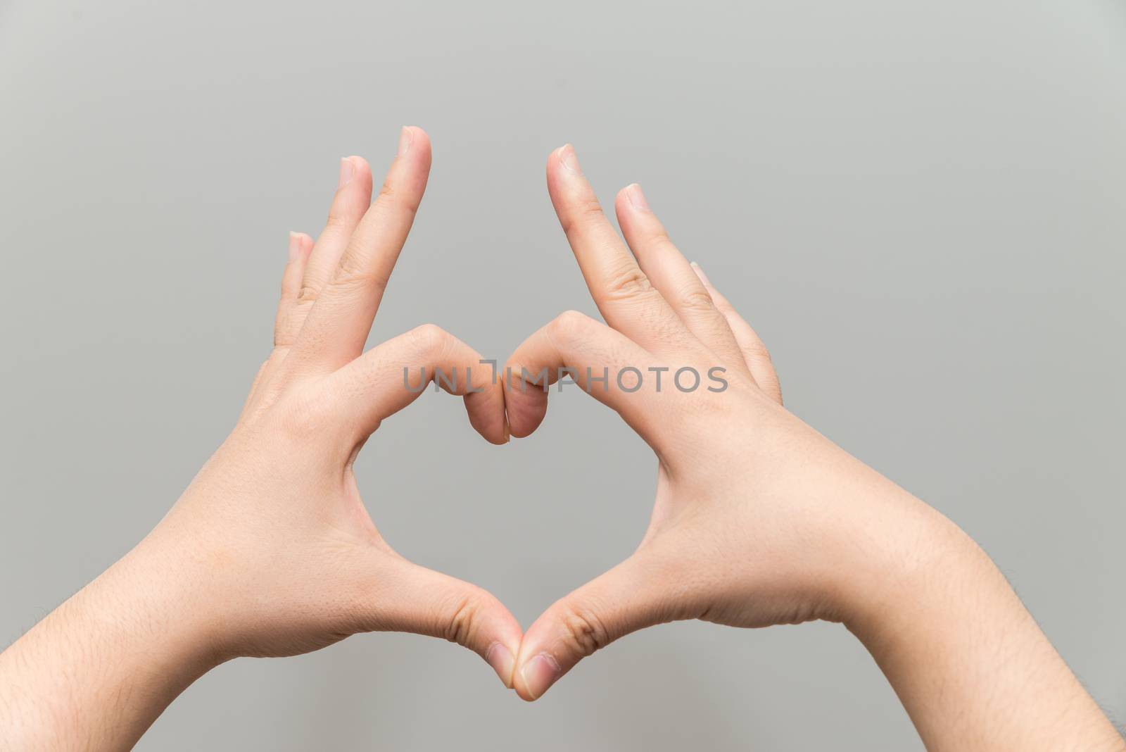 Human hands making a heart shape on light gray background