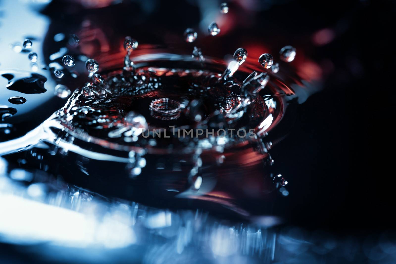 Extremely macro photo of the liquid drop falling on a wet colorful surface