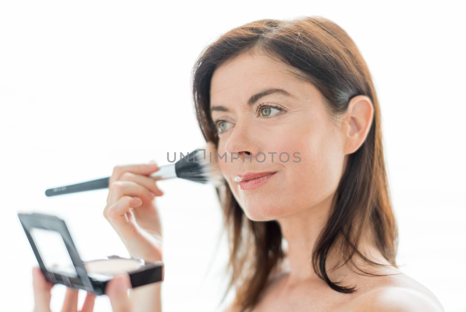 portrait of a beautiful mature lady using professional brush to apply powder on her cheekbones