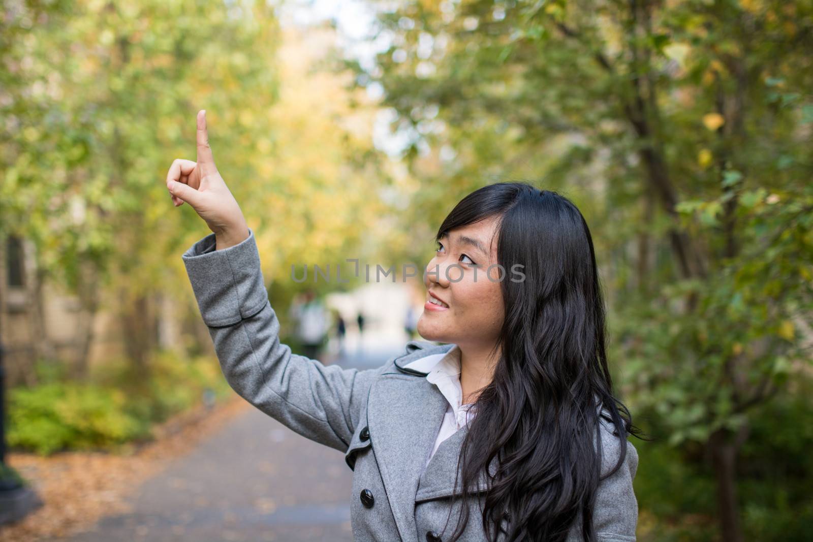 Portrait of young attractive girl pointing at something on the trees at the side of a road