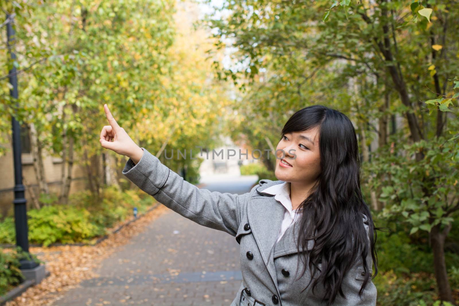 Portrait of young attractive girl pointing at something on the trees at the side of a road