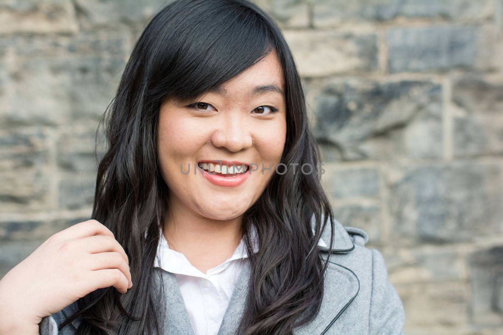 Portrait of beautiful young girl in front of a stone wall looking happy