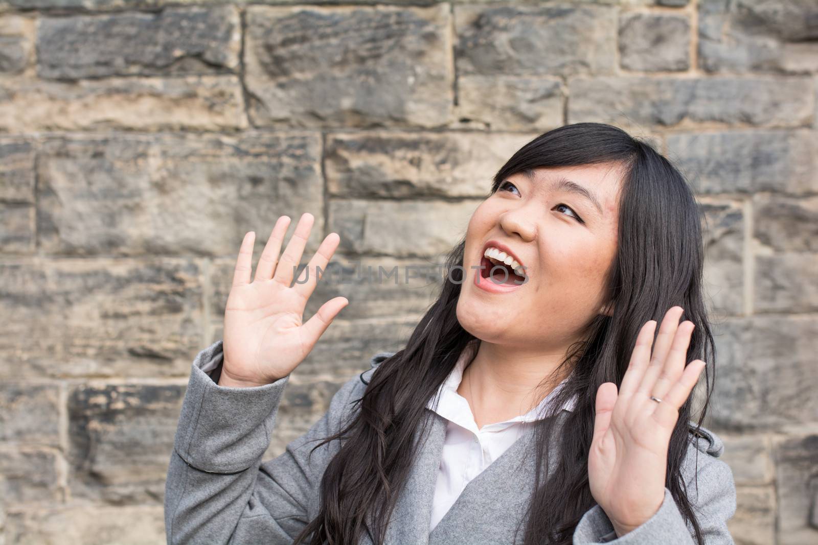 Portrait of pretty young woman laughing out loud in front of a stone wall
