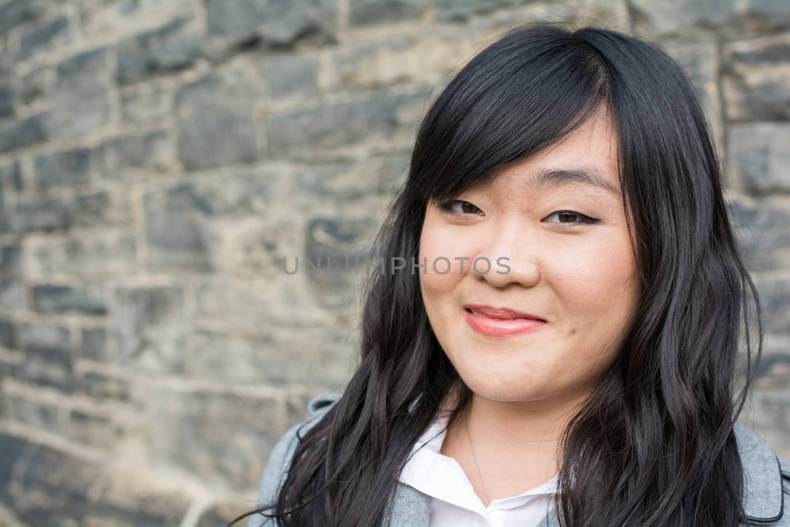 Portrait of beautiful young girl in front of a stone wall looking happy