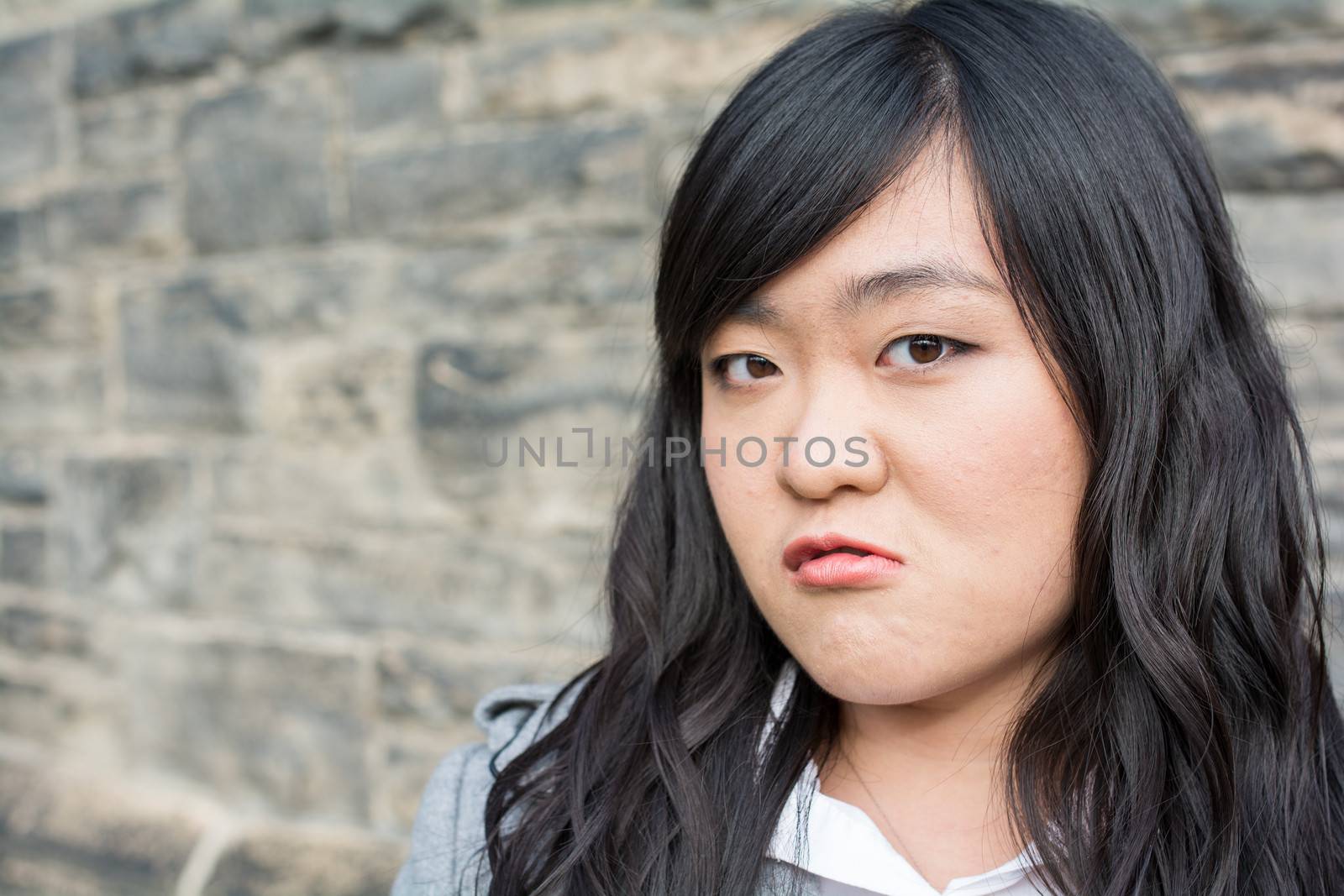 Portrait of young woman in front of a stone wall looking angry
