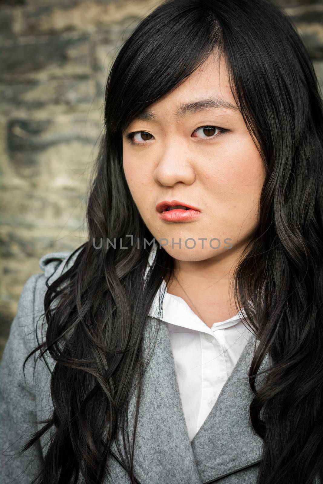 Portrait of young woman in front of a stone wall looking angry