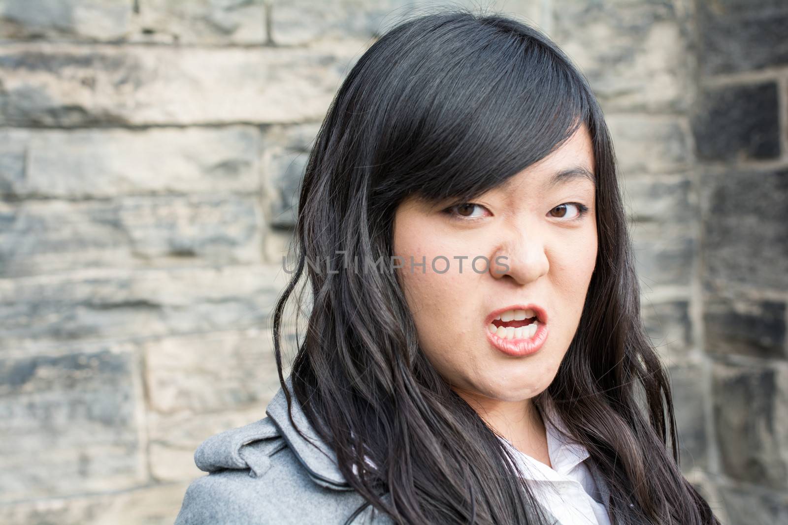 Portrait of young woman in front of a stone wall looking angry