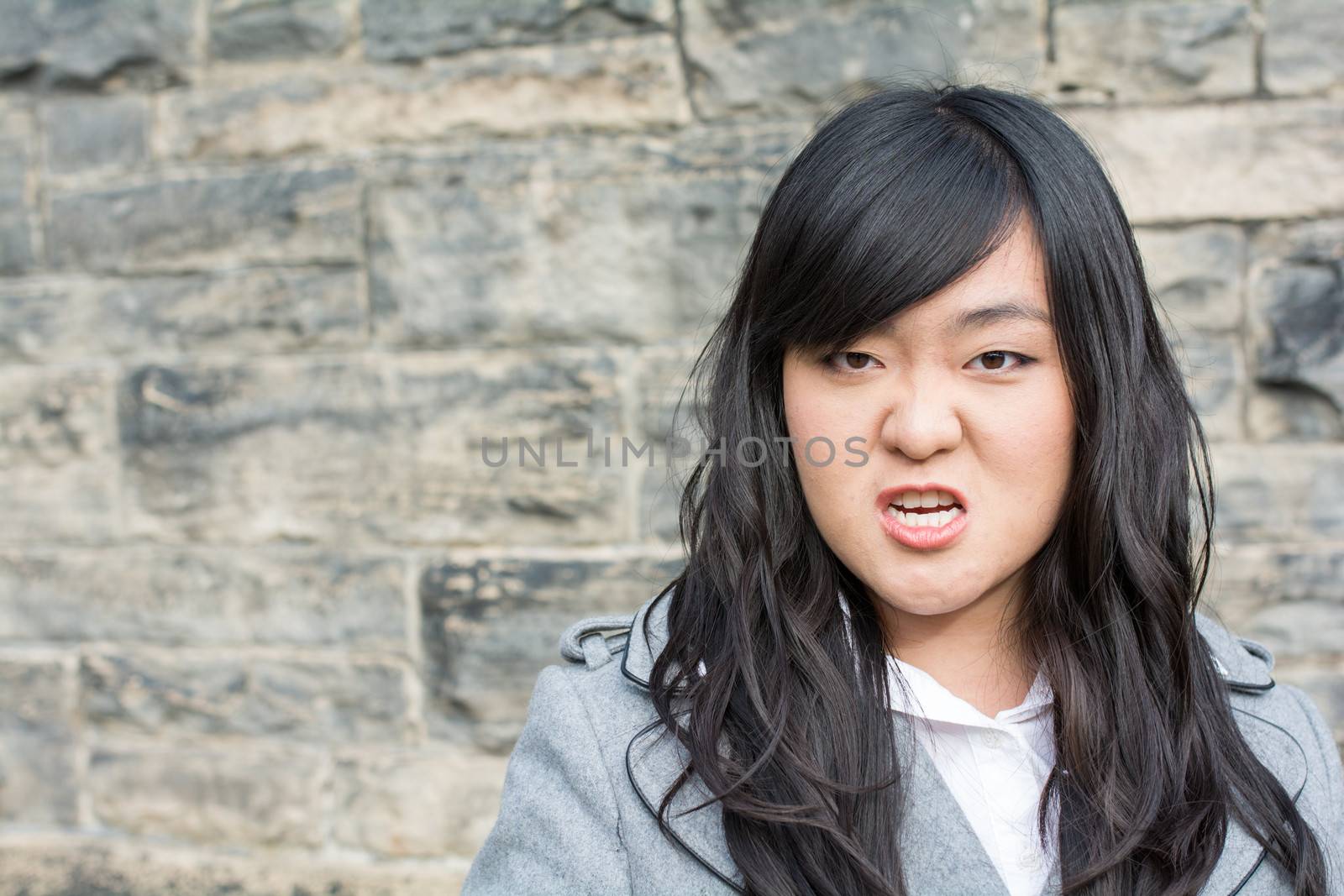 Portrait of young woman in front of a stone wall looking angry