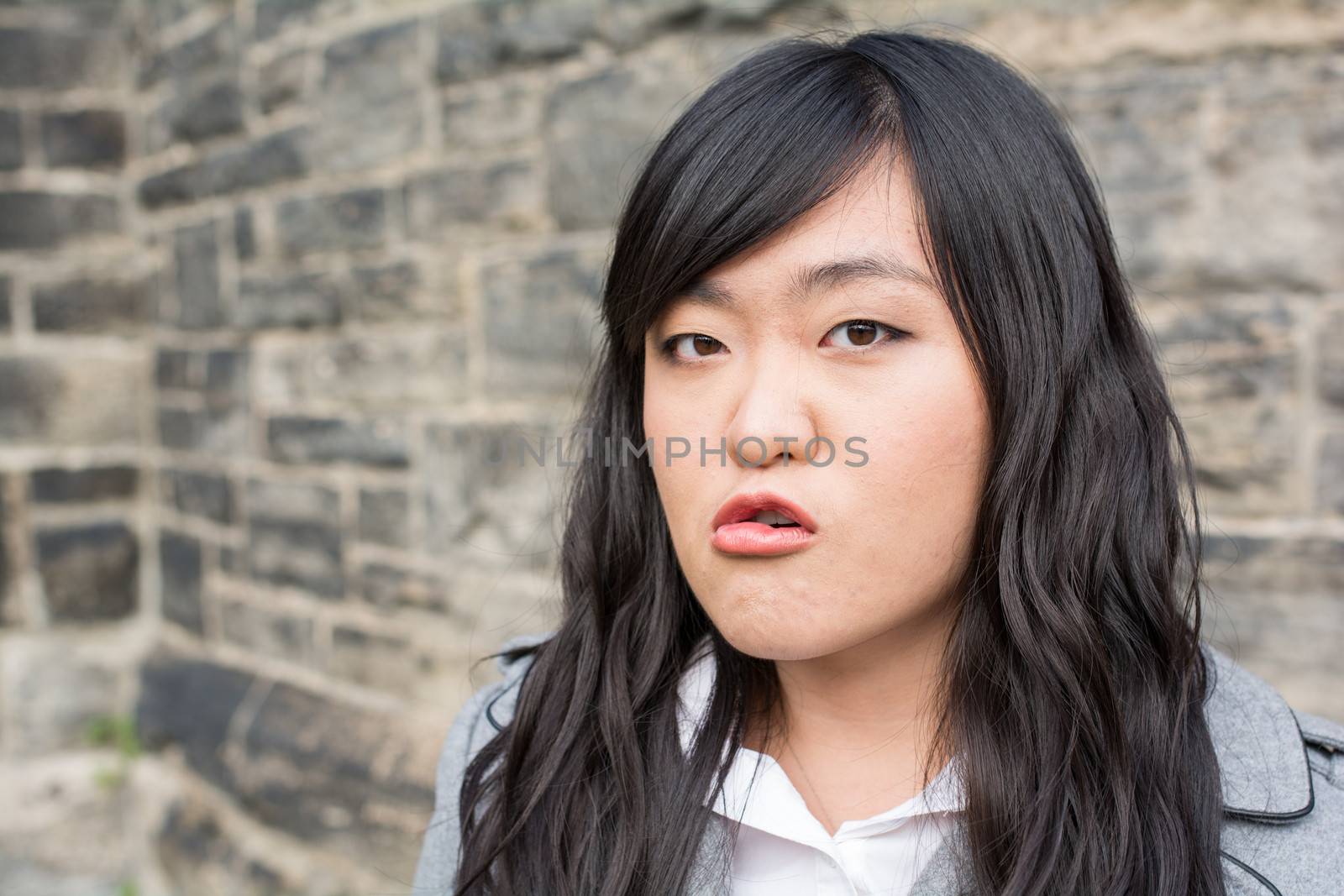 Portrait of young woman in front of a stone wall looking angry