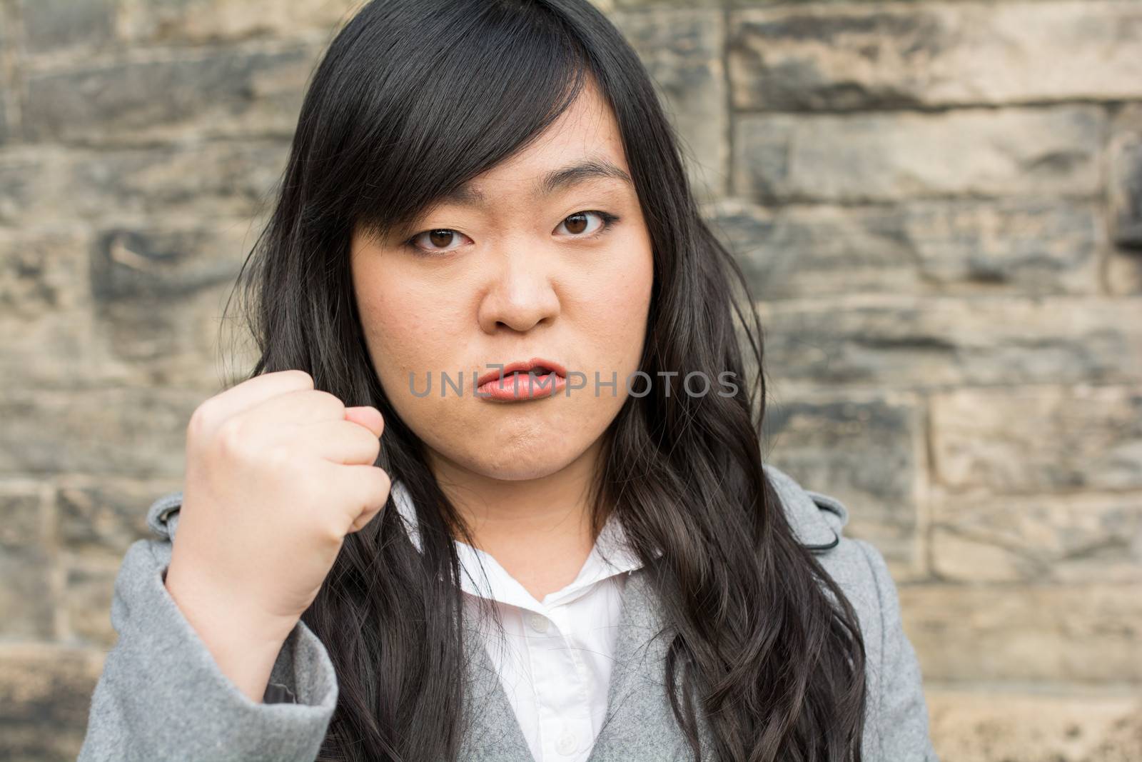 Portrait of young aggressive woman in front of a stone wall looking angry and holding fist