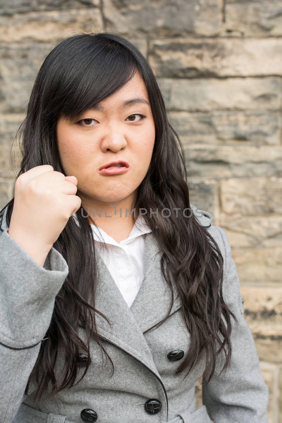 Portrait of young aggressive woman in front of a stone wall looking angry and holding fist