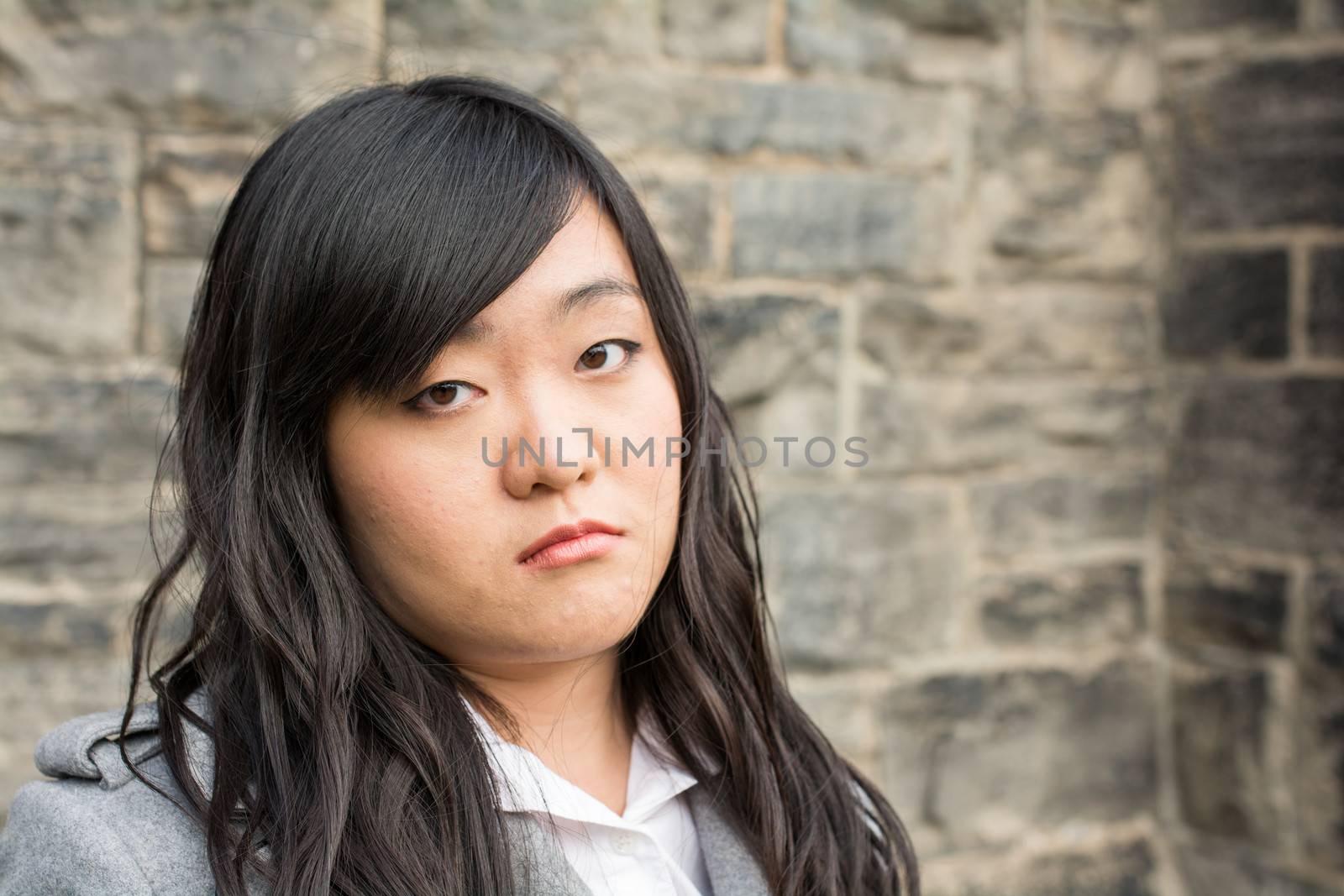 Portrait of young girl in front of a stone wall looking upset
