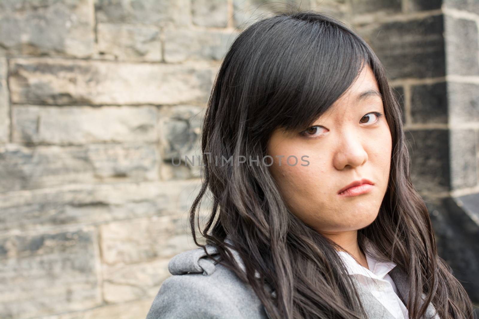 Portrait of young girl in front of a stone wall looking upset