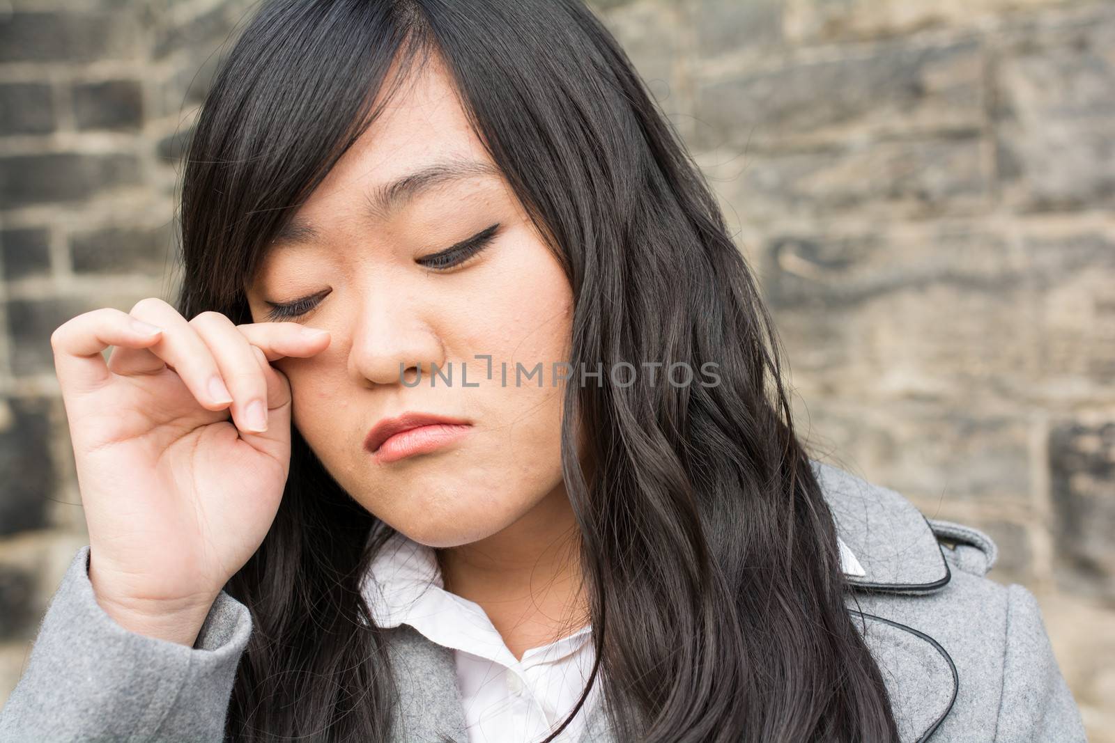 Portrait of young girl in front of a stone wall looking upset and wiping tears