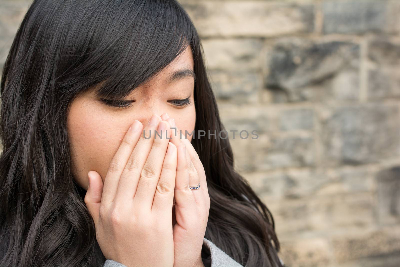 Portrait of young girl in front of a stone wall looking upset and covering mouth