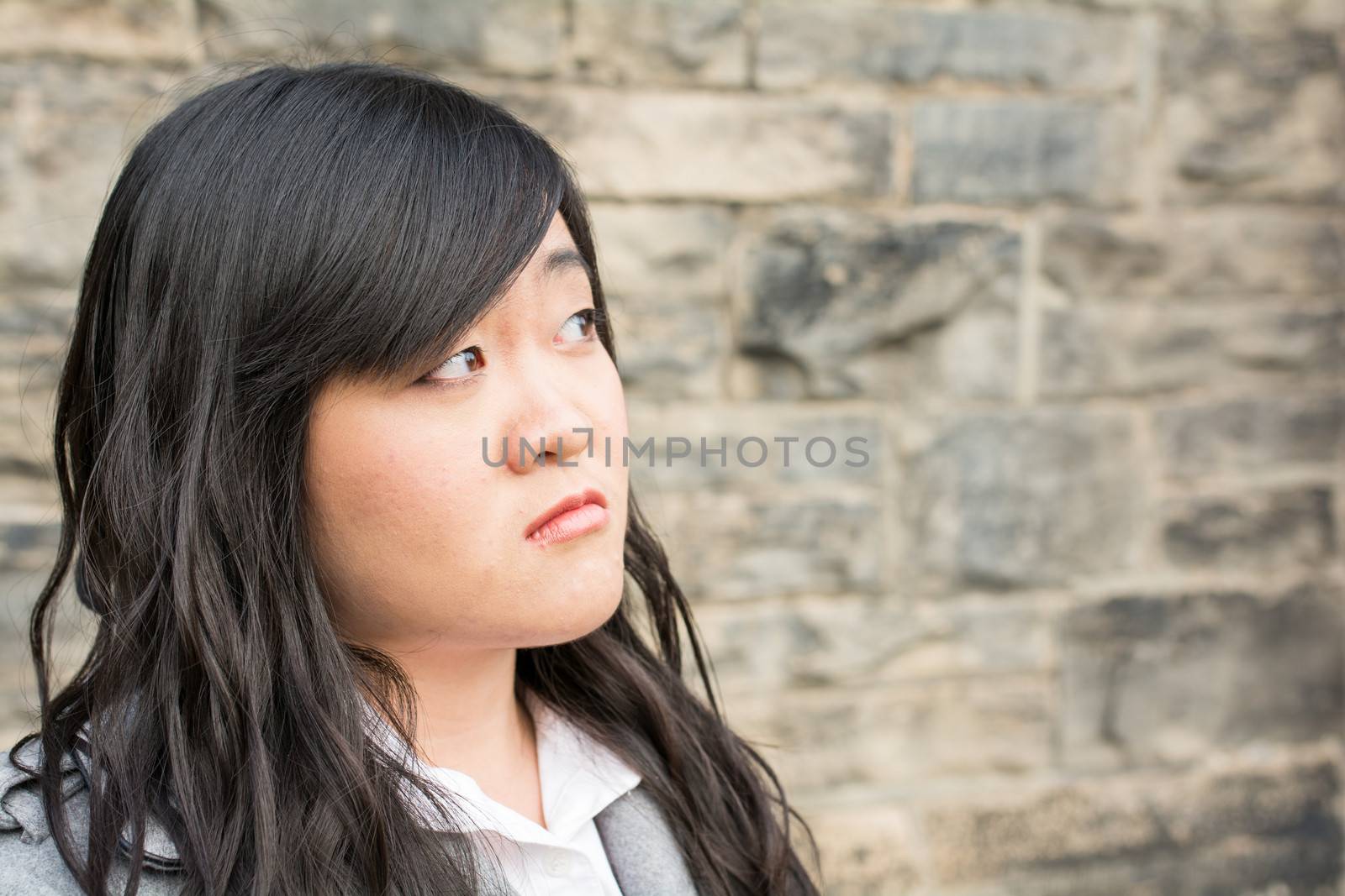 Portrait of young girl in front of a stone wall looking upset and looking away