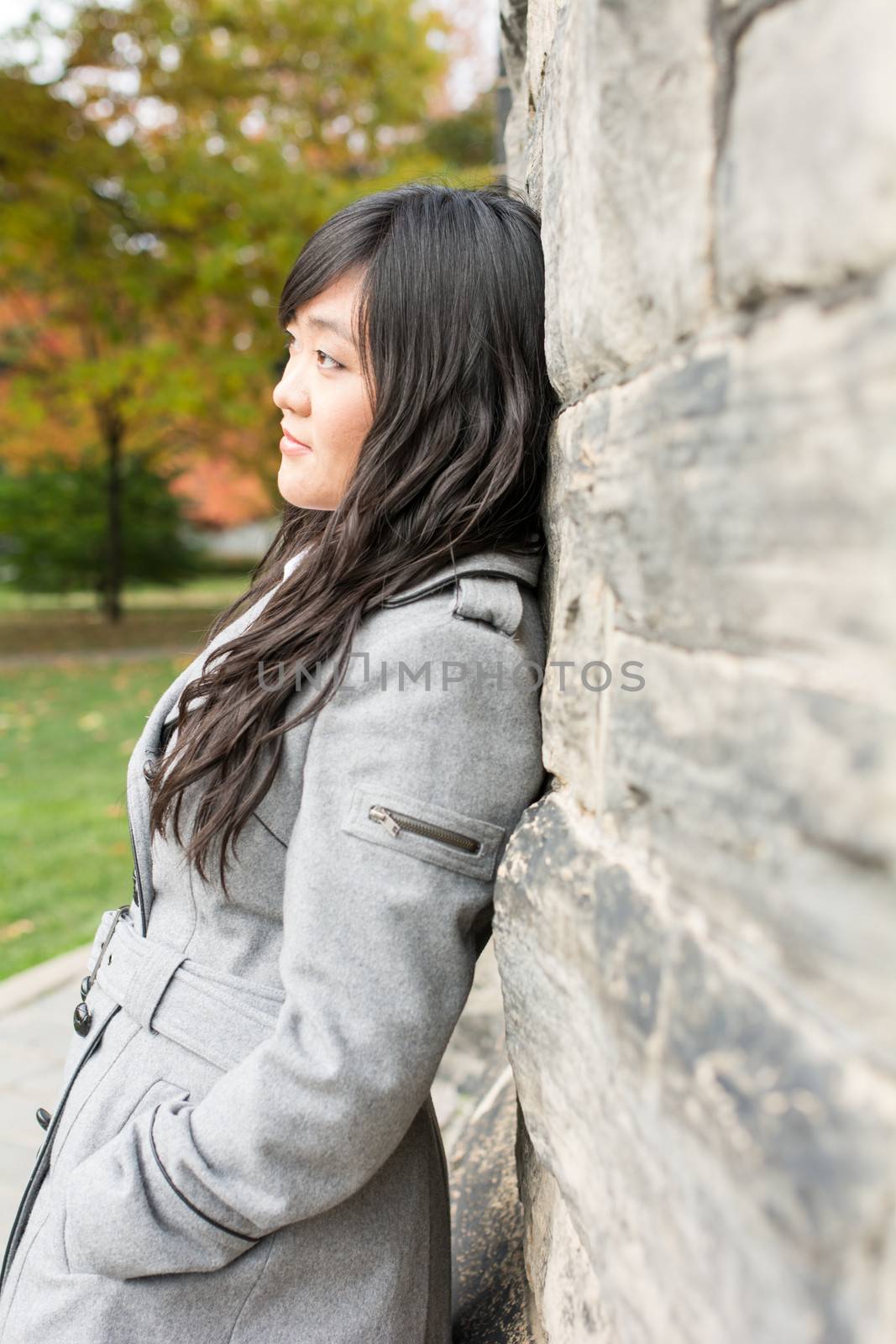 Portrait of young woman standing back against a stone wall looking hopeful