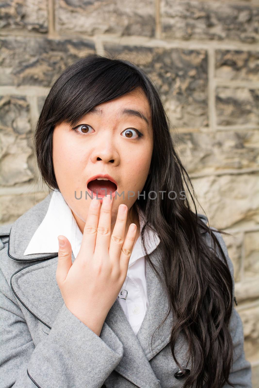 Portrait of attractive young woman looking surprised and trying to cover mouth