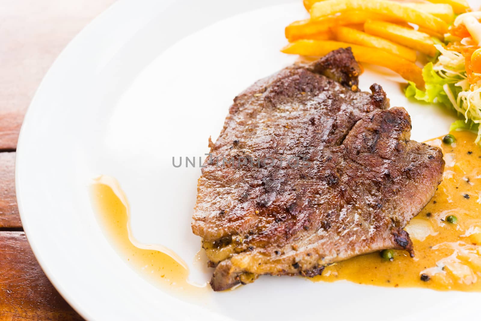 beef steak on white dish with salad french fries and pepper gravy sauce on wood table