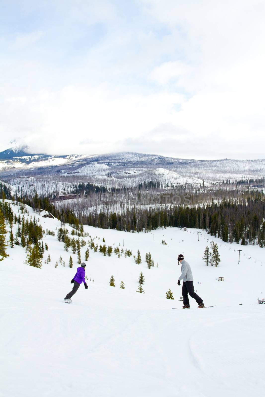 A couple snowboards down some groomed ski runs at a mountain resort.