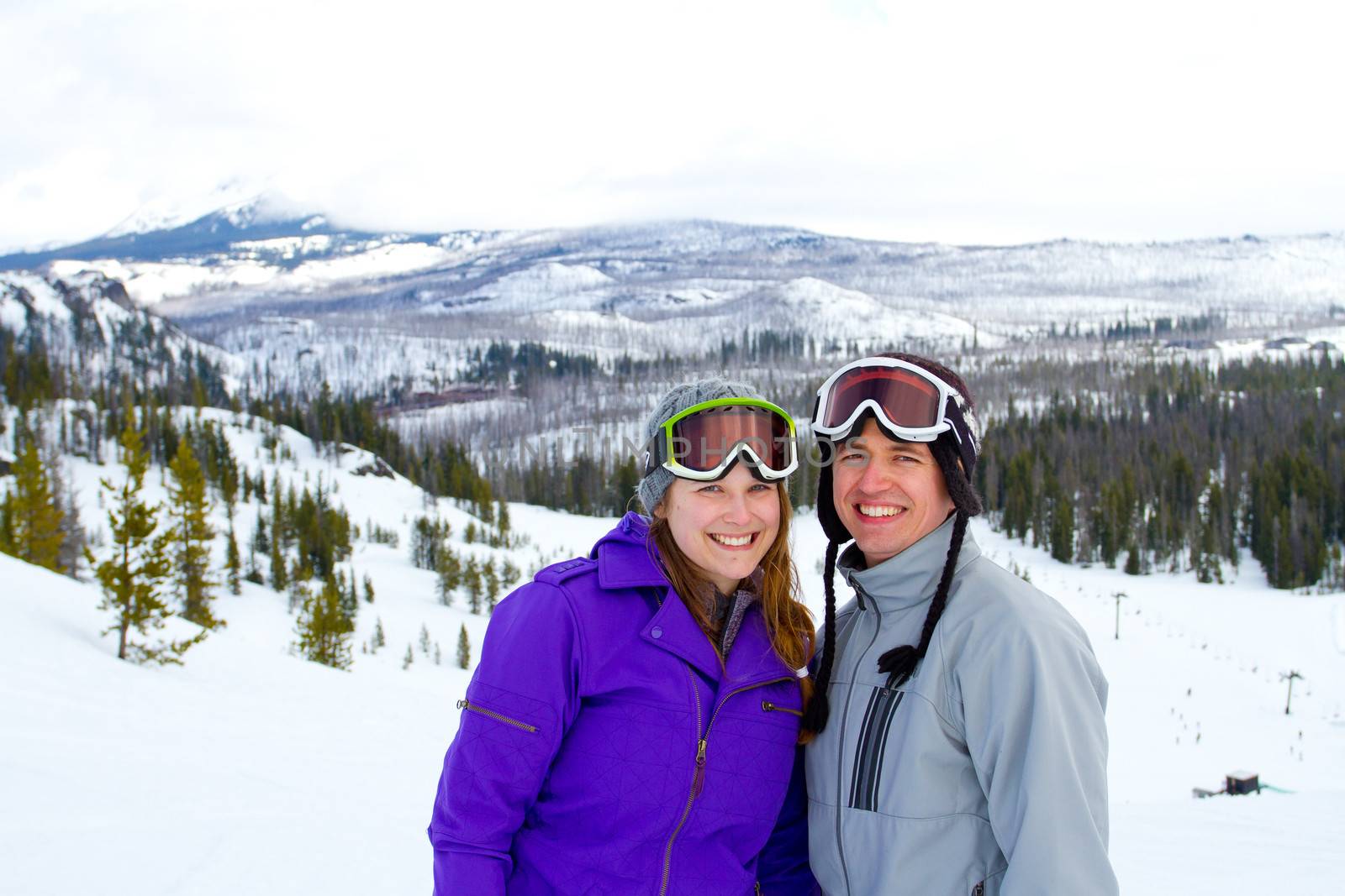 A happy couple together on the mountain resort in the snow for a day of skiing and snowboarding.