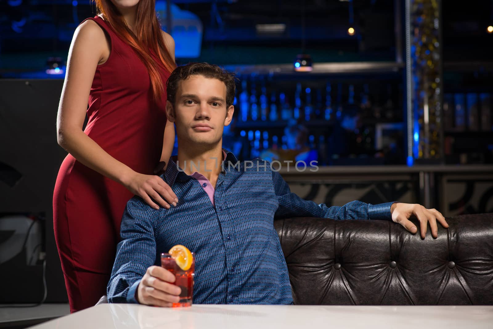 Portrait of a successful man in a nightclub, sitting on the couch, next to a woman in a red dress