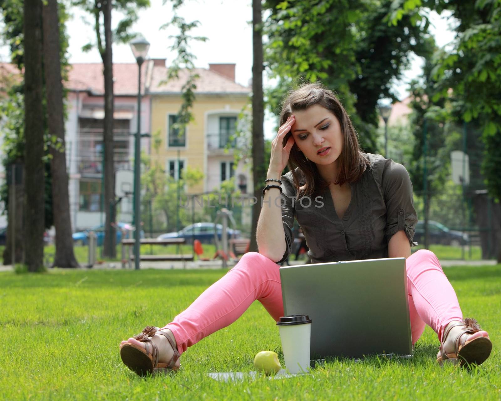 Young woman thinking in front of a laptop outside in an urban park.