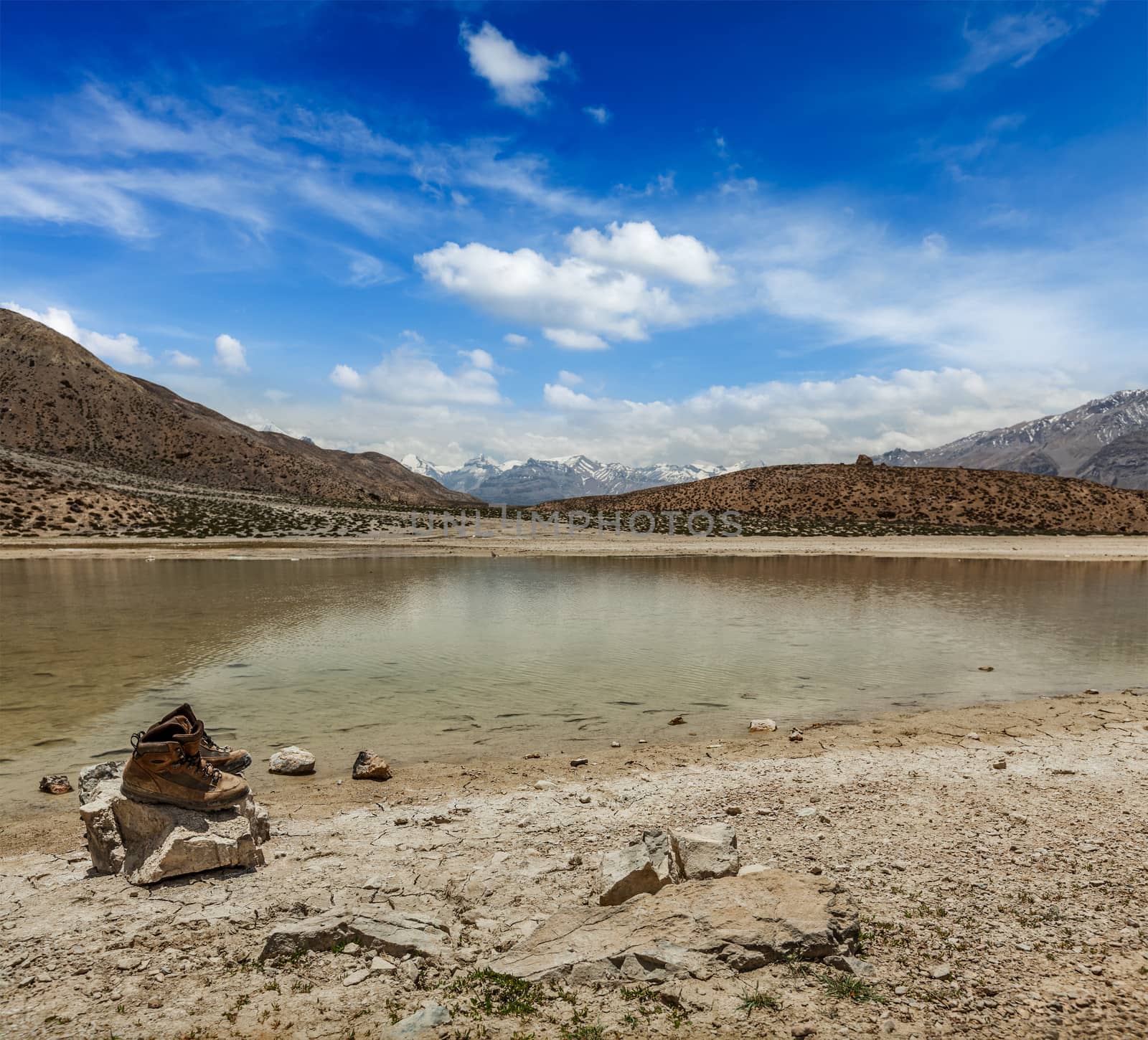 Mountain trekking concept background - trekking hiking boots at mountain lake in Himalayas