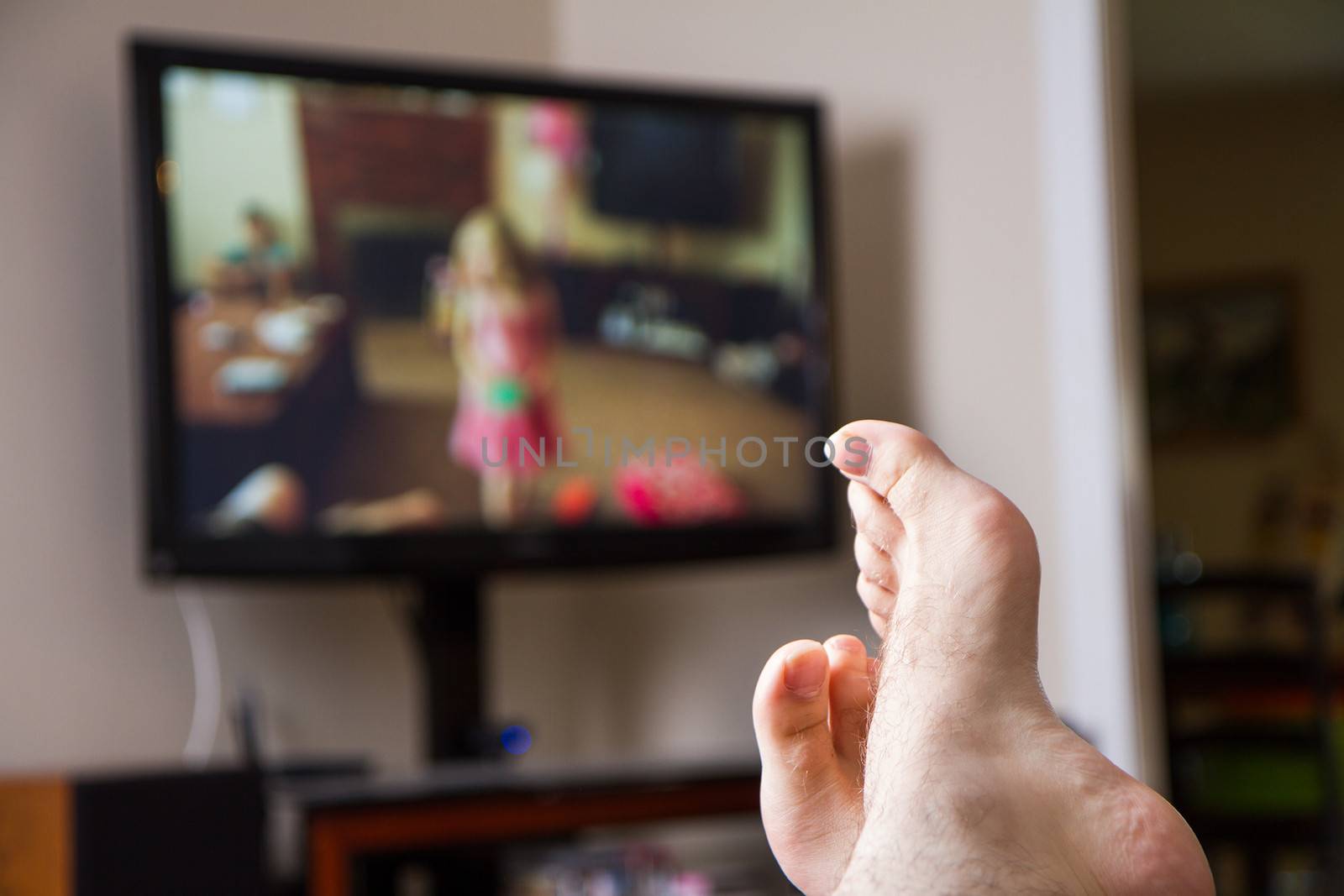 Shallow depth of field with feet in focus of a guy watching family movies on the TV in the background