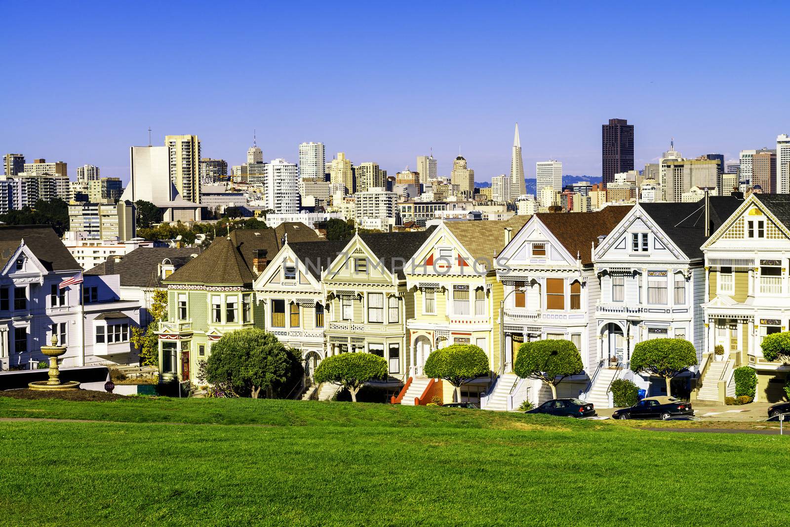 The Painted Ladies of San Francisco, California sit glowing amid the backdrop of a sunset and skyscrapers. 