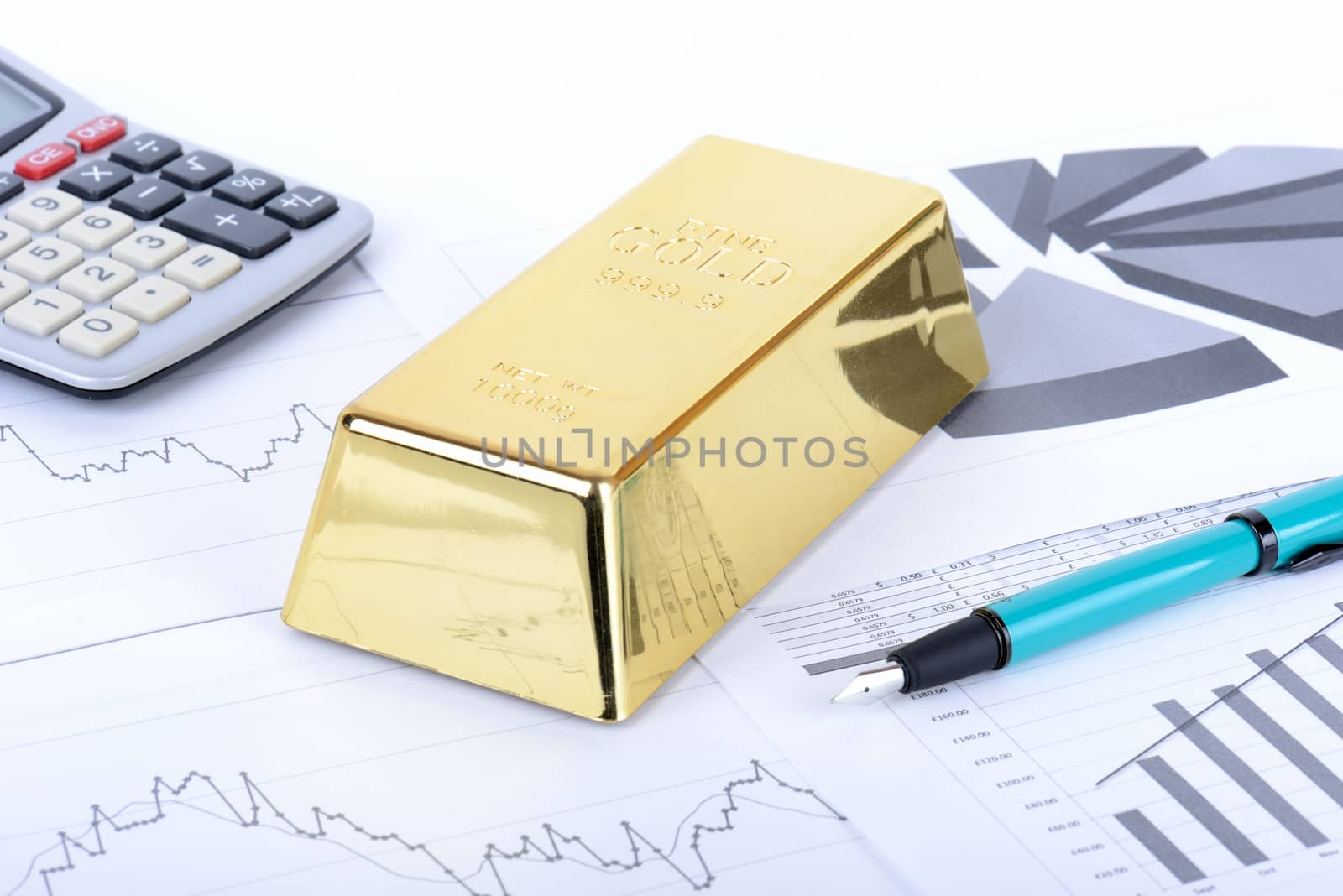 Gold bar on stock figures with calculator and pen