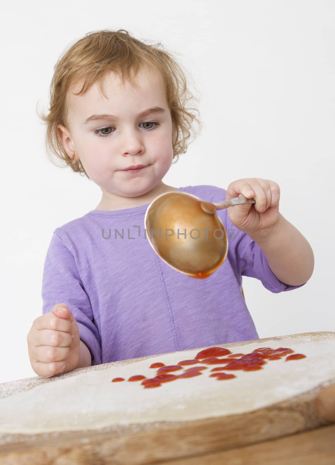 child putting sieved tomatoes on dough. studio shot in grey background