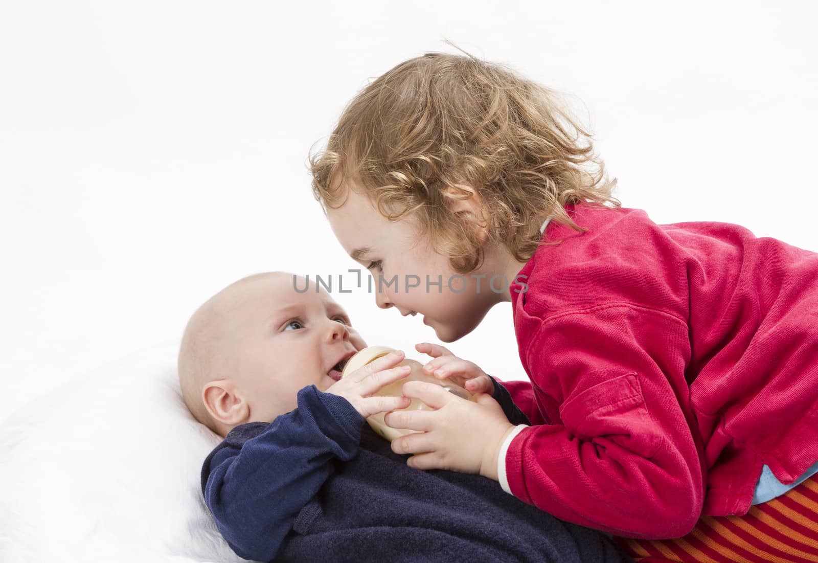 cute girl playing with her baby brother in light grey background. Studio shot