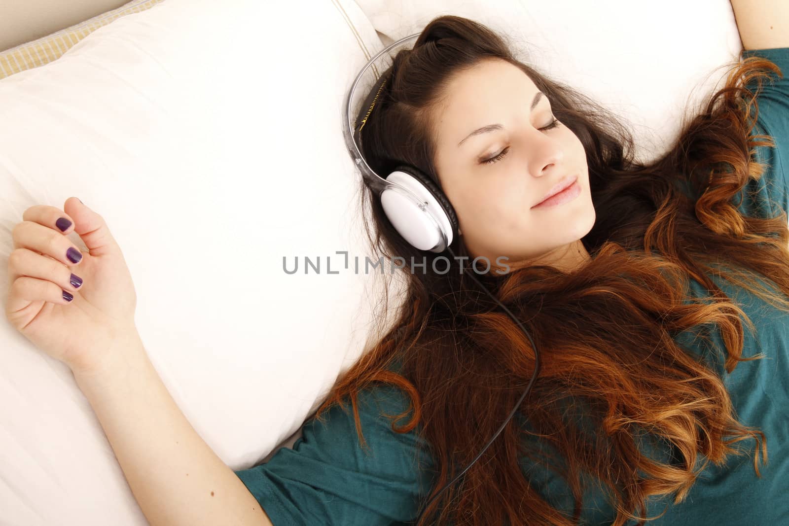 A young adult woman listening music with headphones in bed.