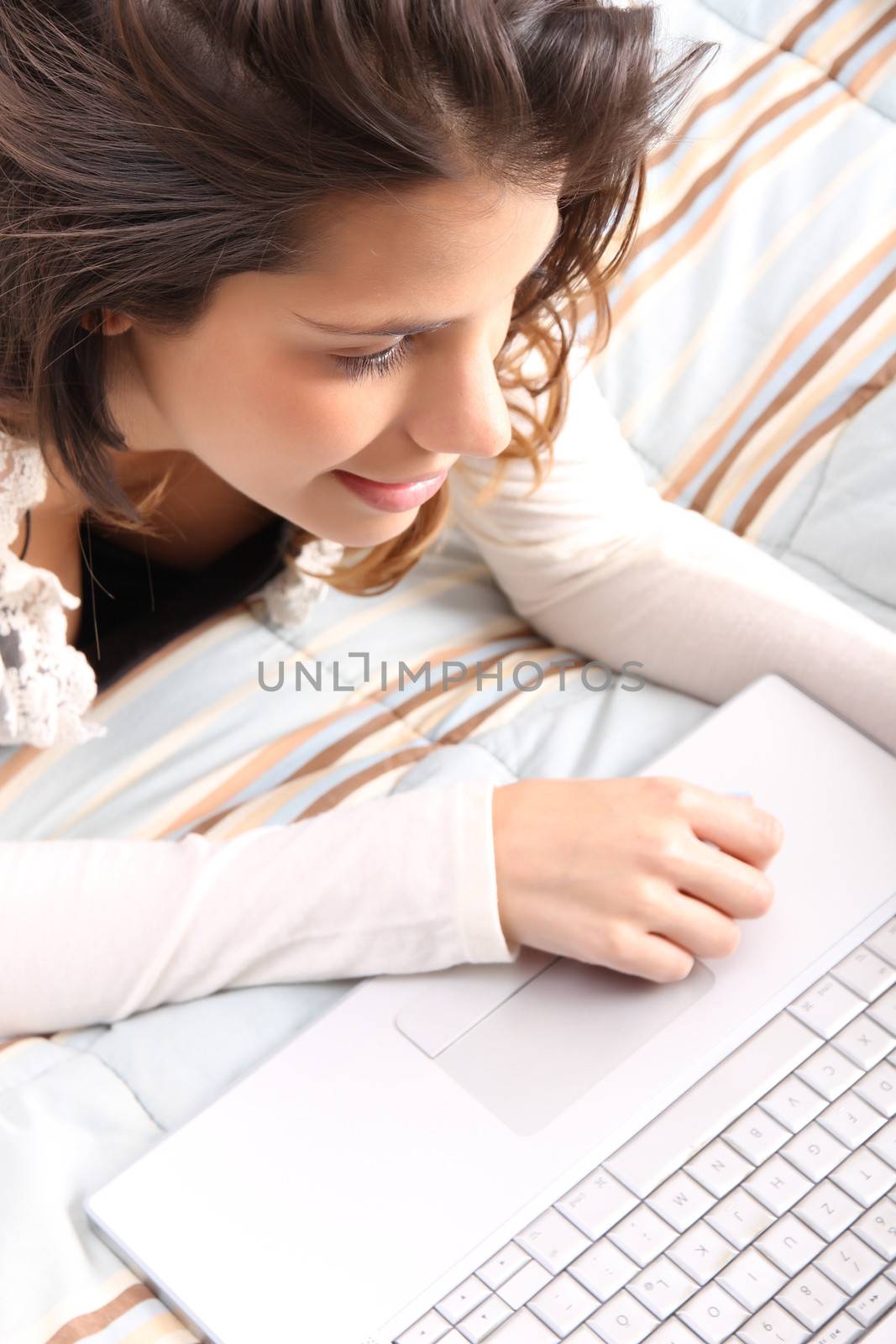 A young girl laying on the bed and surfing on the Internet with a Laptop.