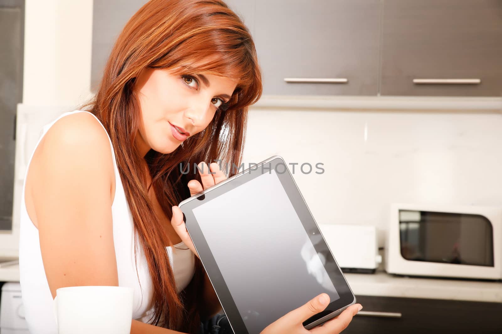 A young woman showing a Tablet PC in the kitchen.