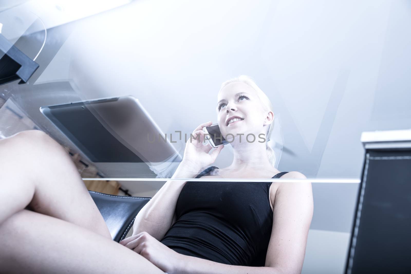 A Girl sitting at a glass desk on the phone.