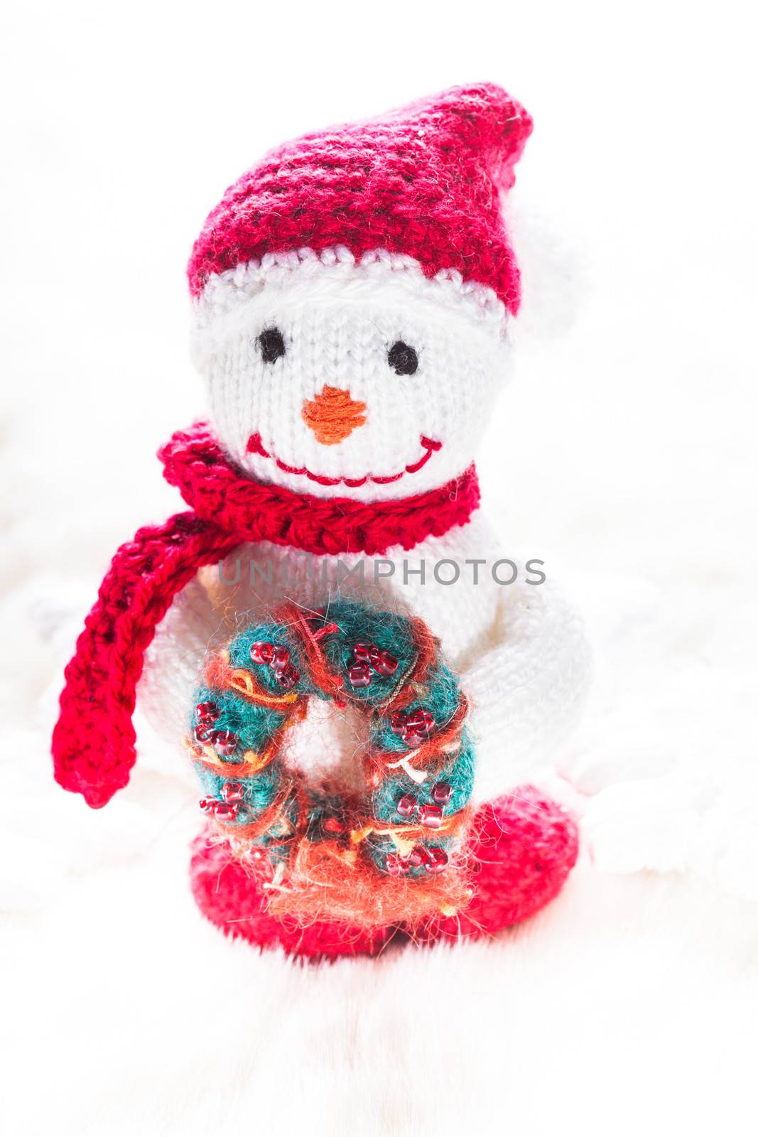 Knitted snowman with christmas wreath on white snow