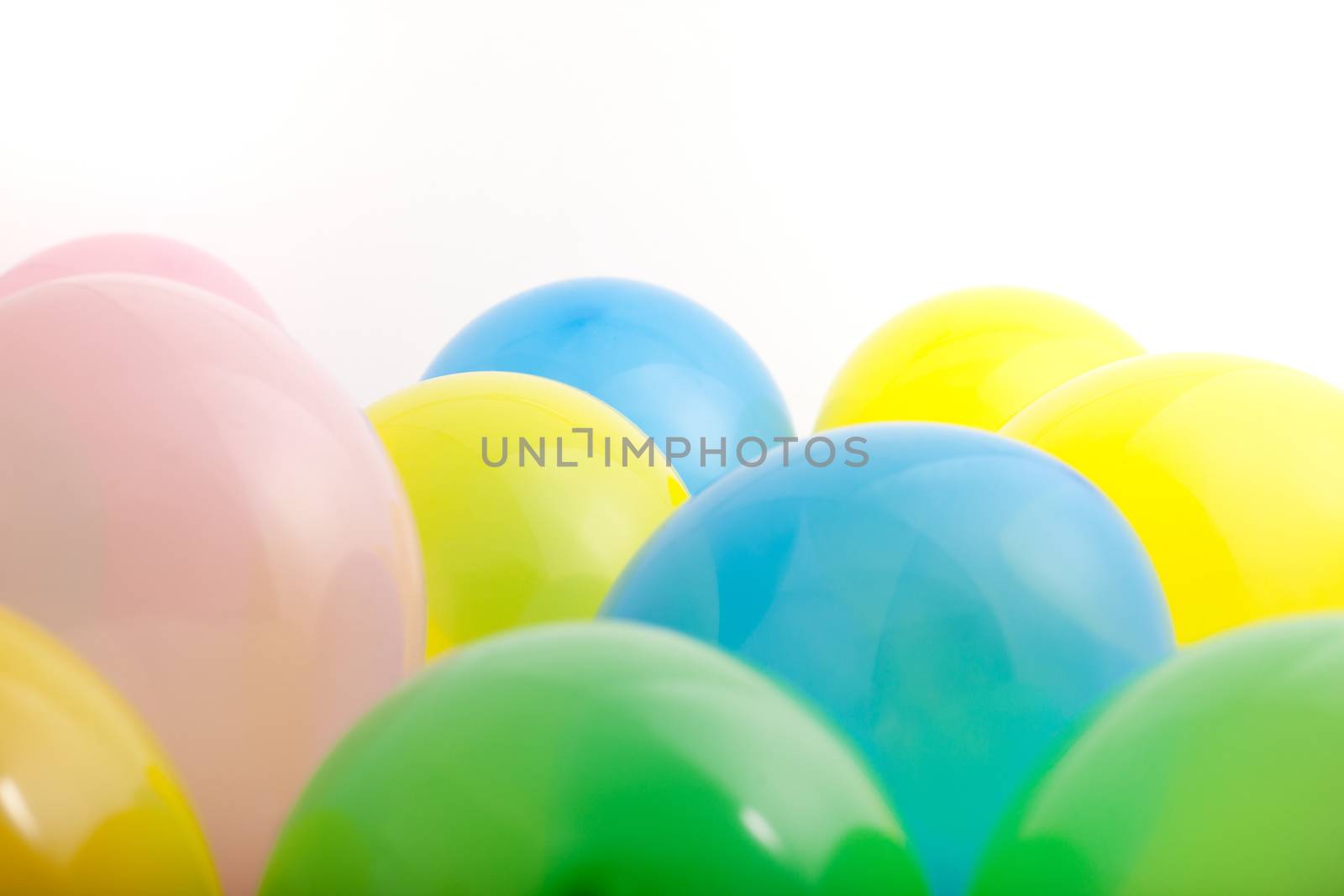 Multicoloured party balloons in green, blue, yellow and pink in a random scatter on a white background with copyspace