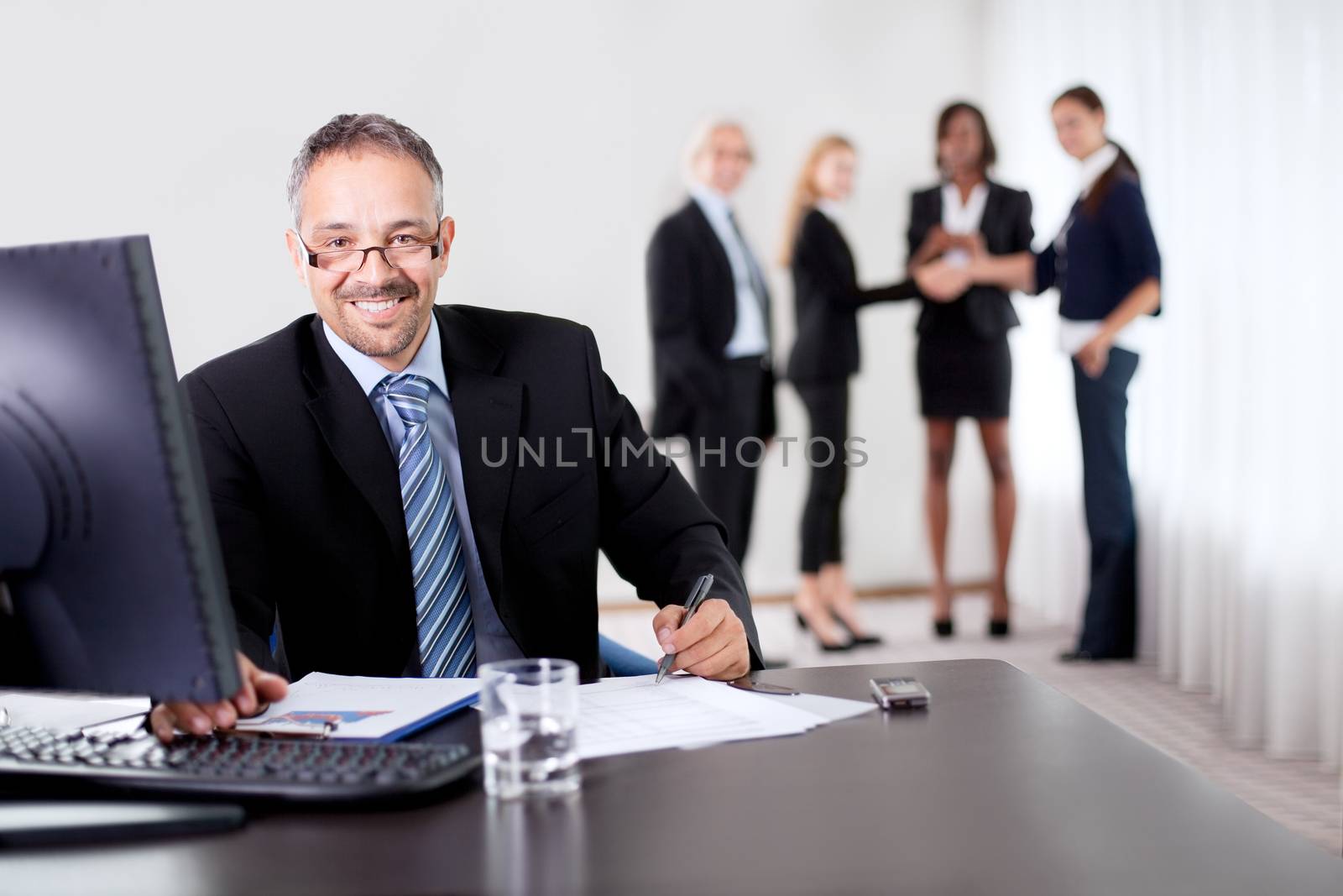 Successful businessman doing some paperwork during a meeting - smiling at the camera